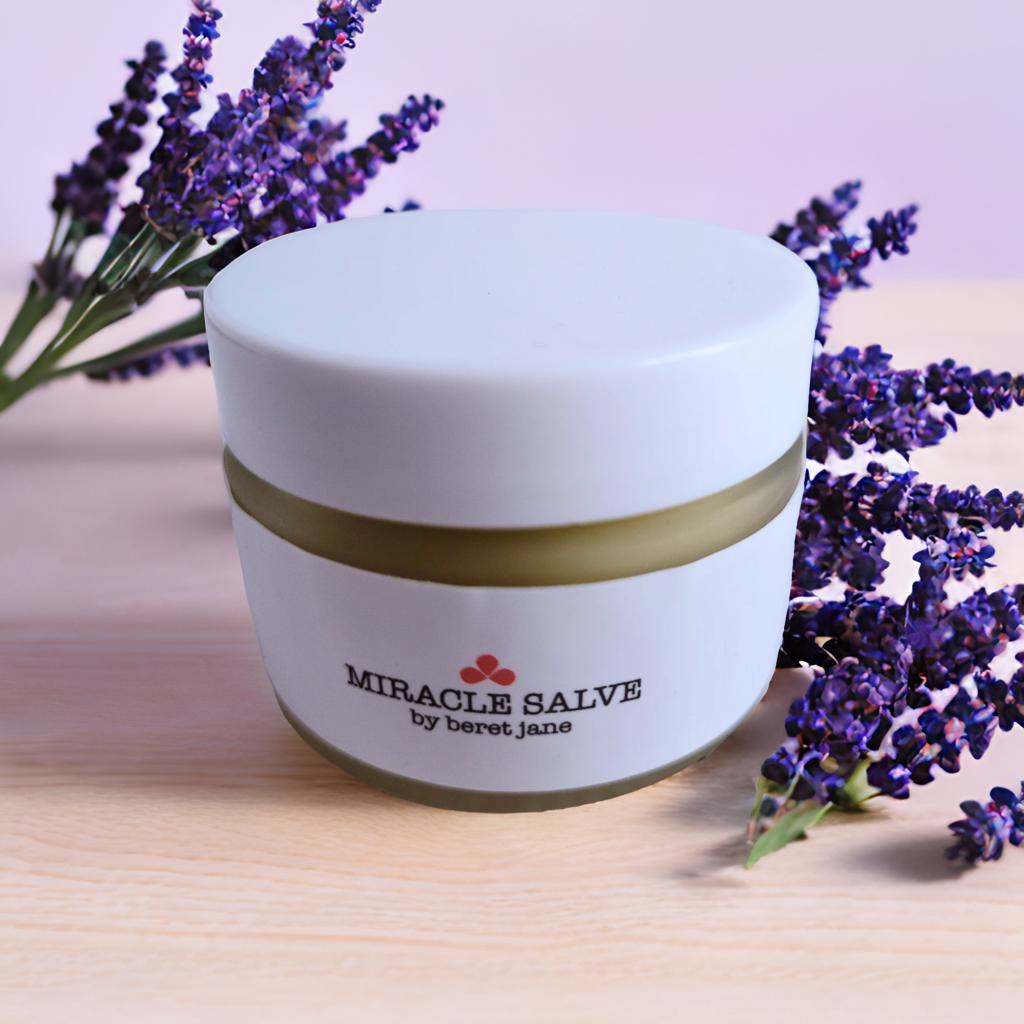 Jar of Beret Jane Miracle Salve on a table beside fresh lavender